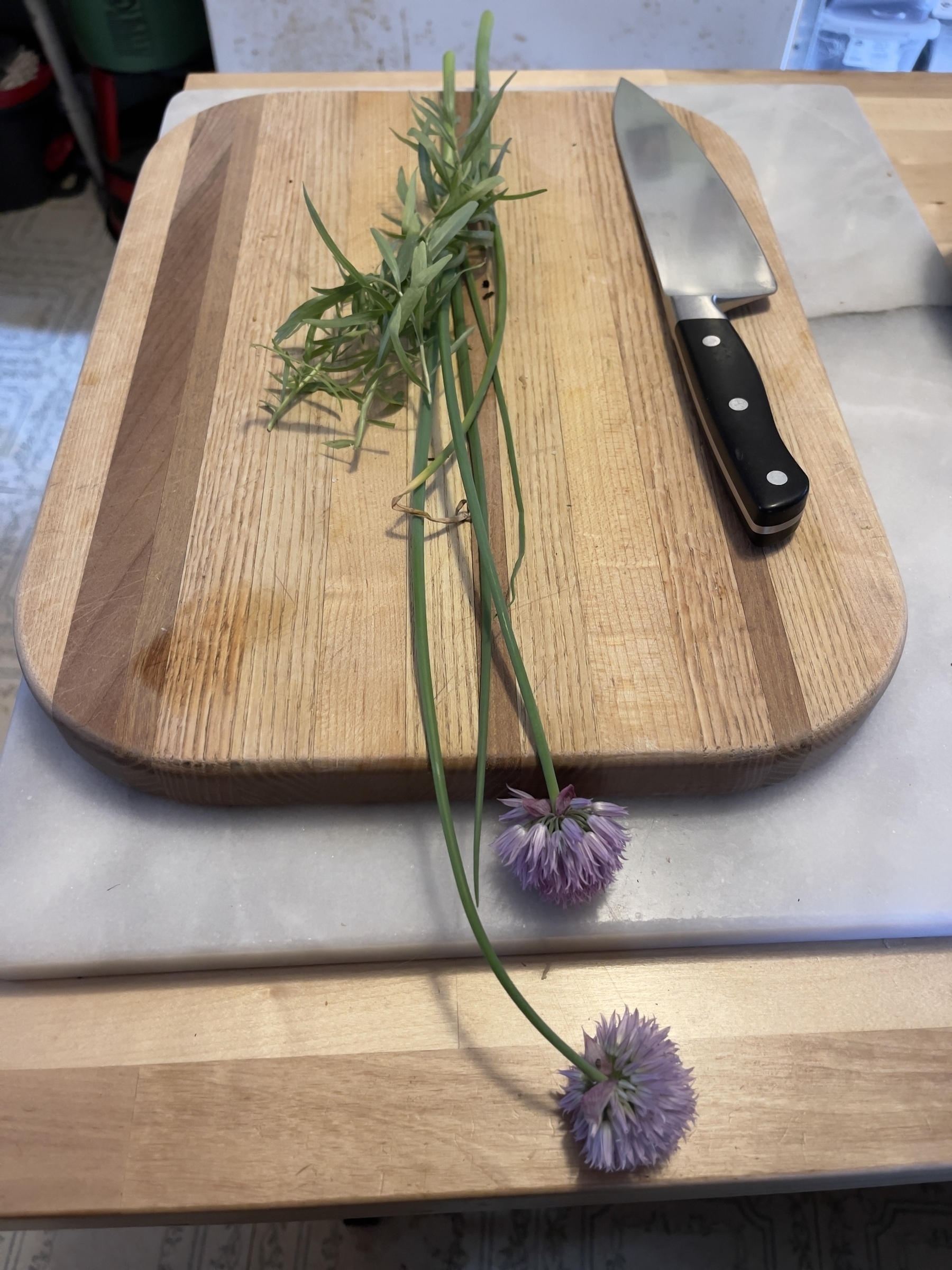 Tarragon and chive blossoms on a cutting board with knife.