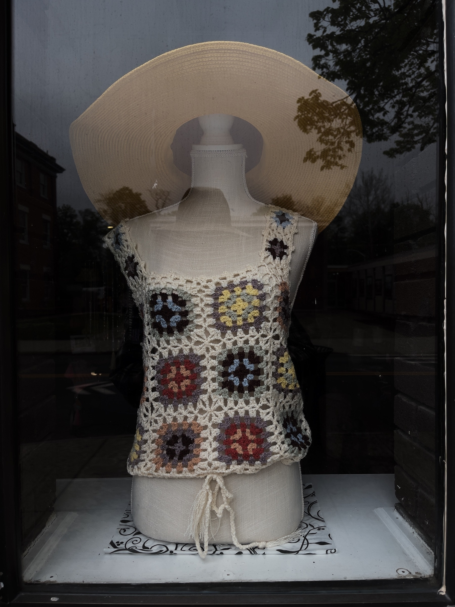 Crocheted woman’s top and wide brim sun hat on a mannequin bust in a shop window.