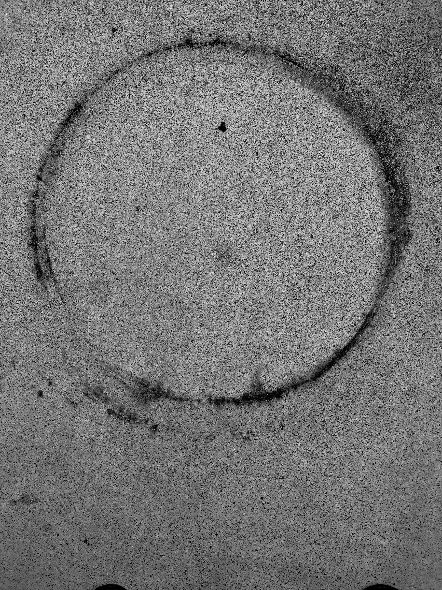 Circular rust stain on concrete pavement. Black and white.