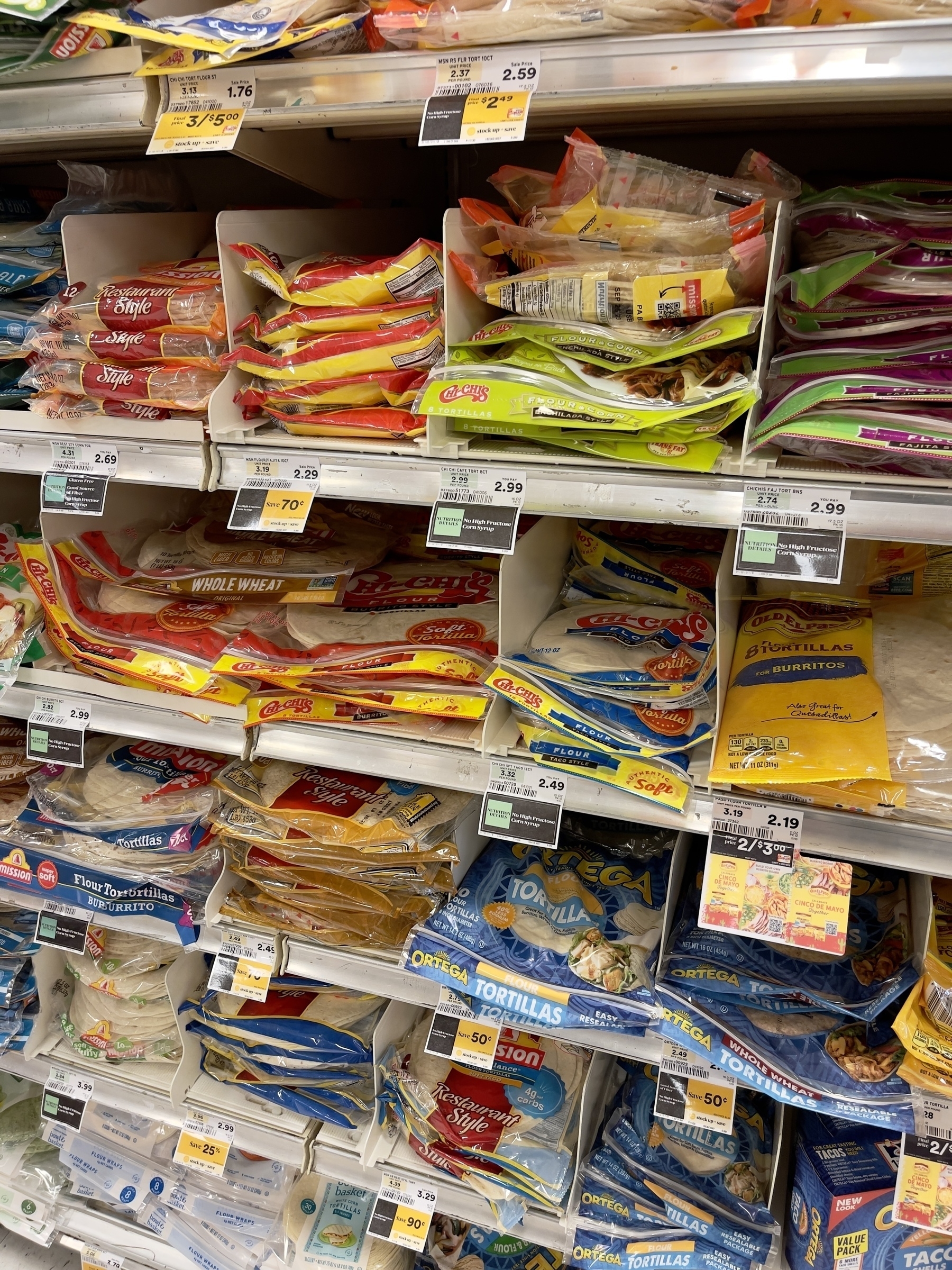 Various kinds of flatbread wrapped in colorful plastic on shelves of a grocery store. Color.