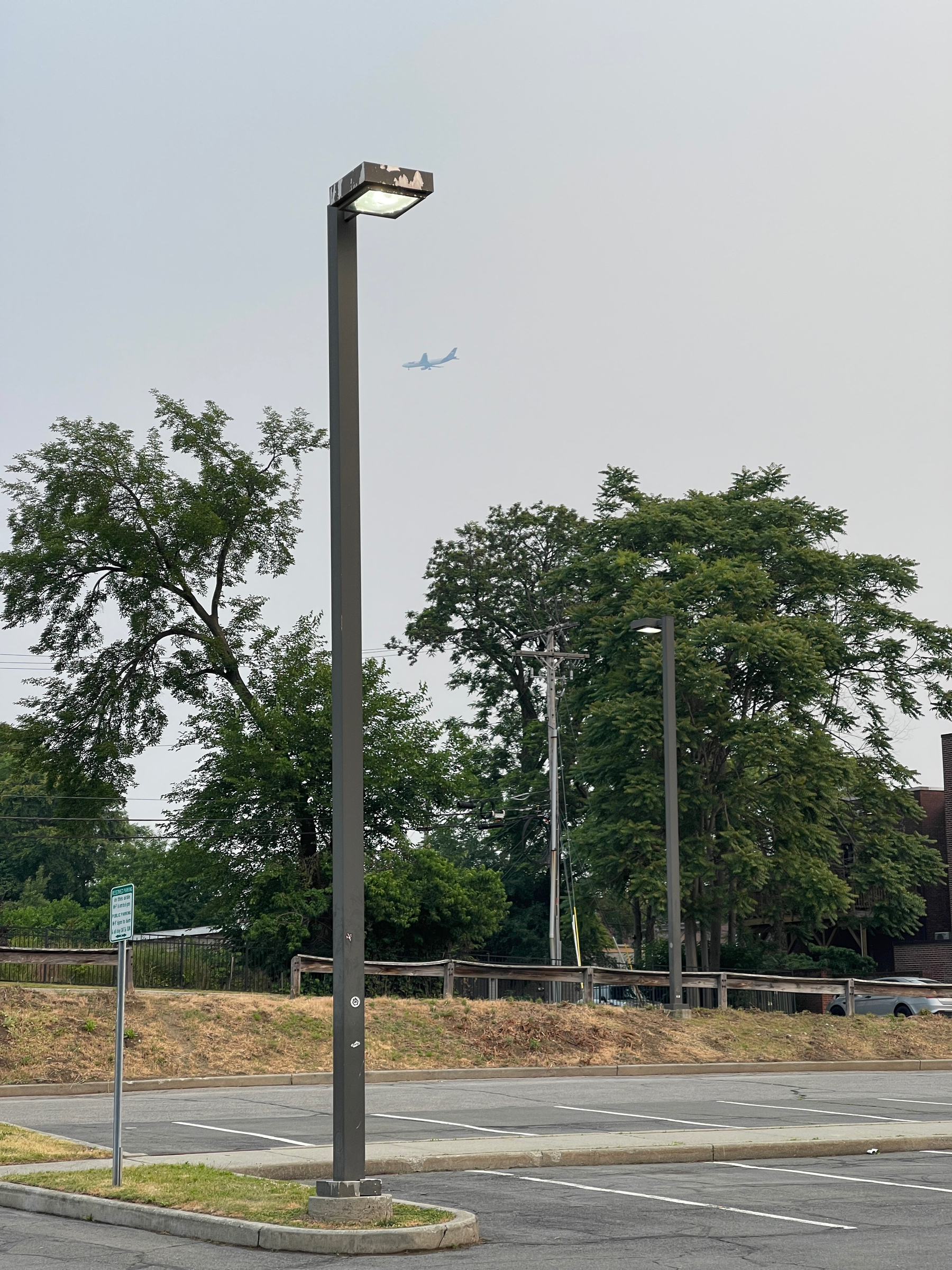 Parking lot, light pole, jet passenger plane flying by in the distance.