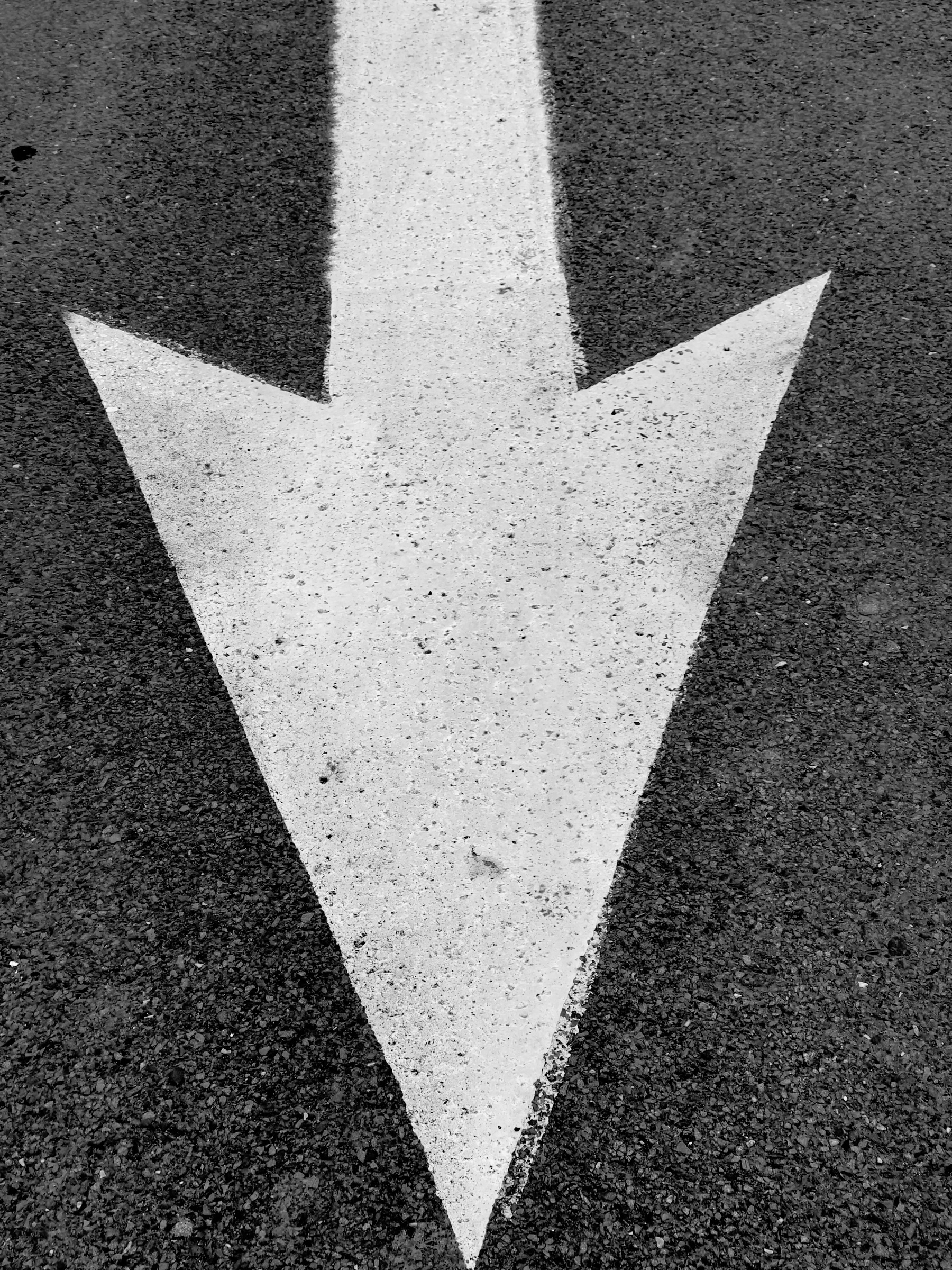 White painted directional arrow on asphalt. Black and white.