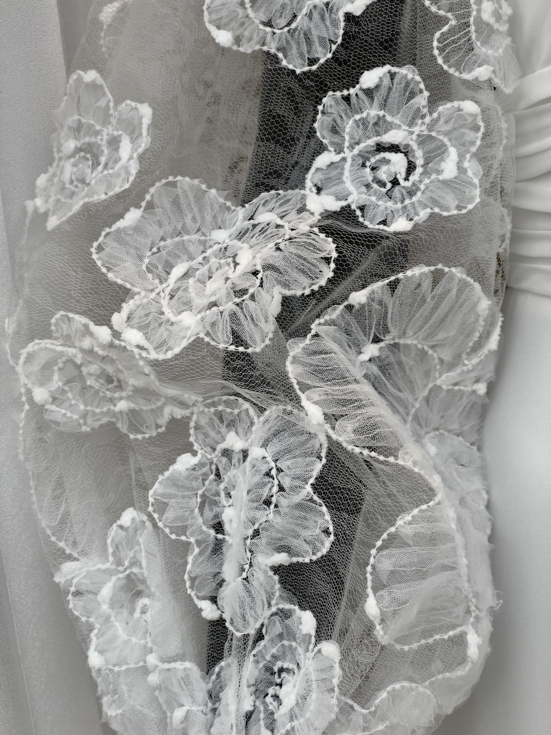 Lace poppy like flowers on sleeve of white wedding gown. Monochrome.