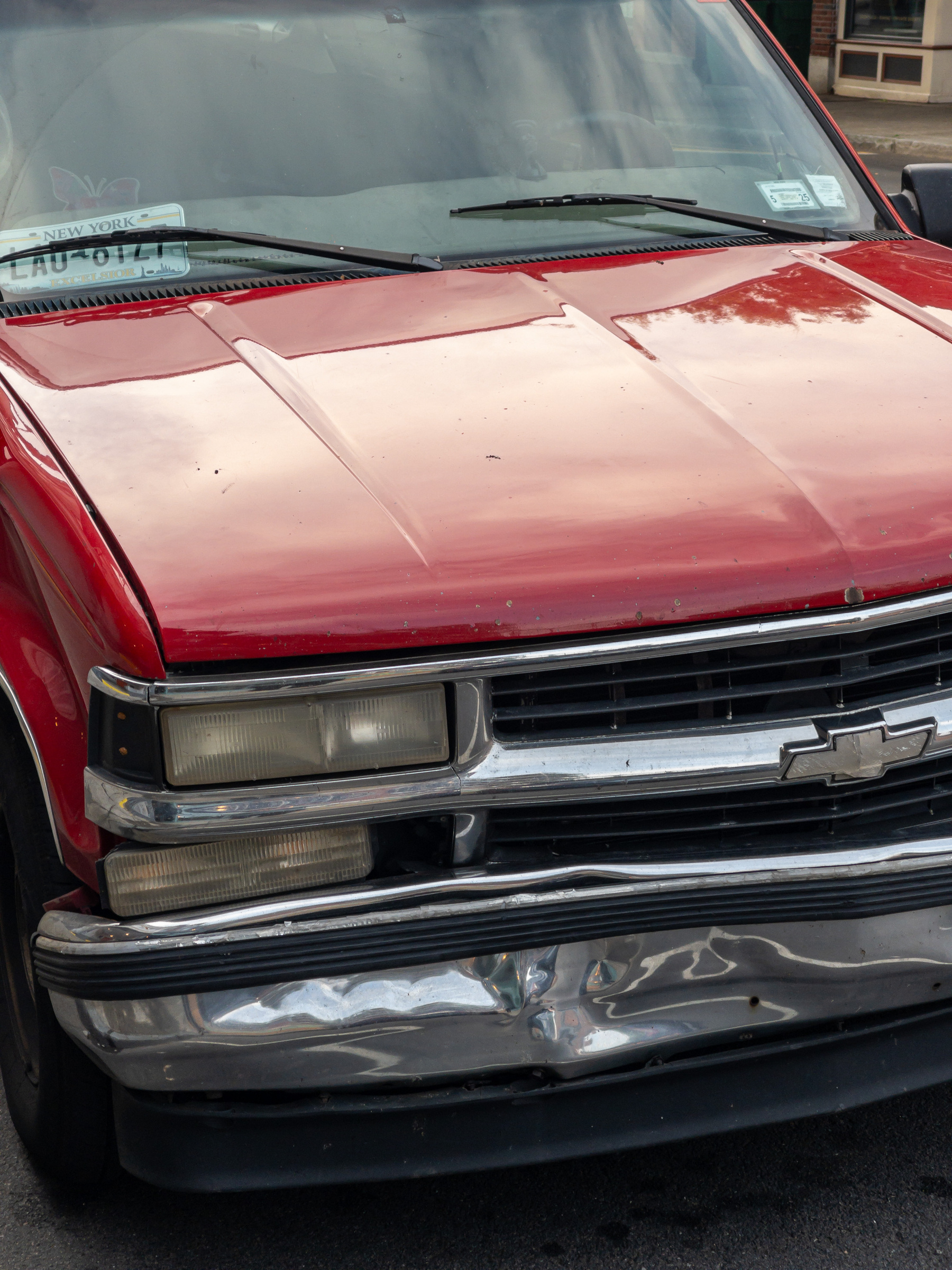 Dented chrome fender of an old red Chevrolet pickup truck.