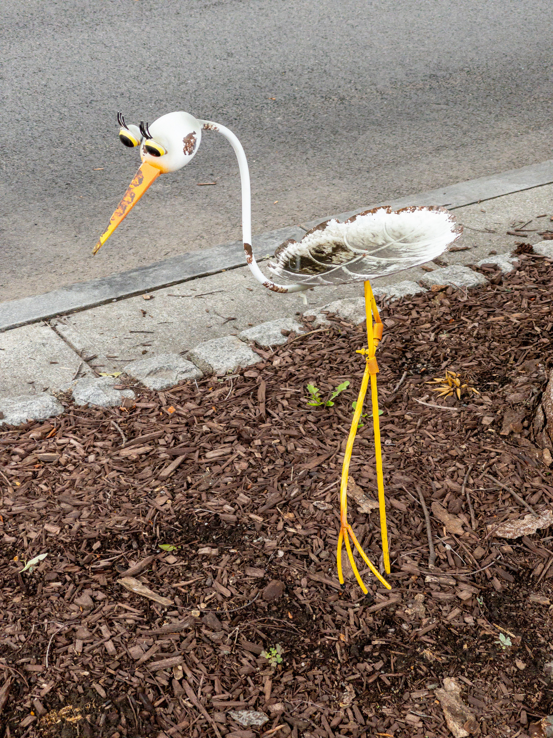 Metal sculpture stork in median by the street.