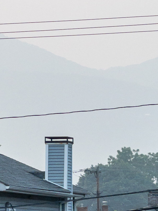 Closeup of mountains obscured by smoke haze from Canadian wildfires. Roof and chimney in the foreground.