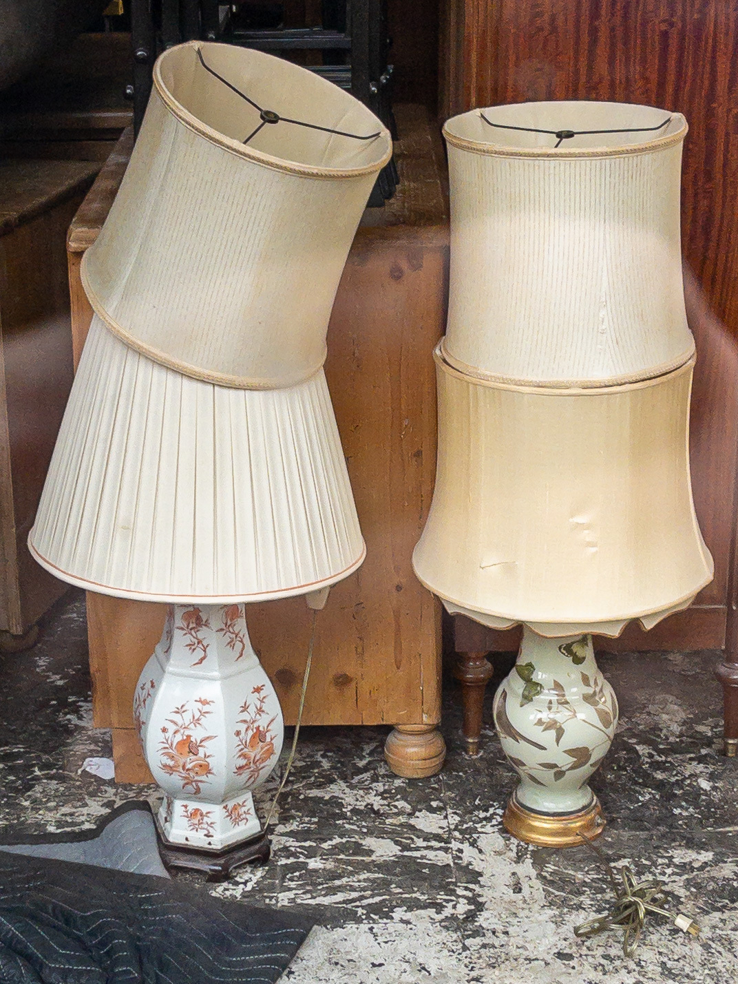 Two antique lamp bases, each with a lamp shade attached and second lamp shade piled on top.