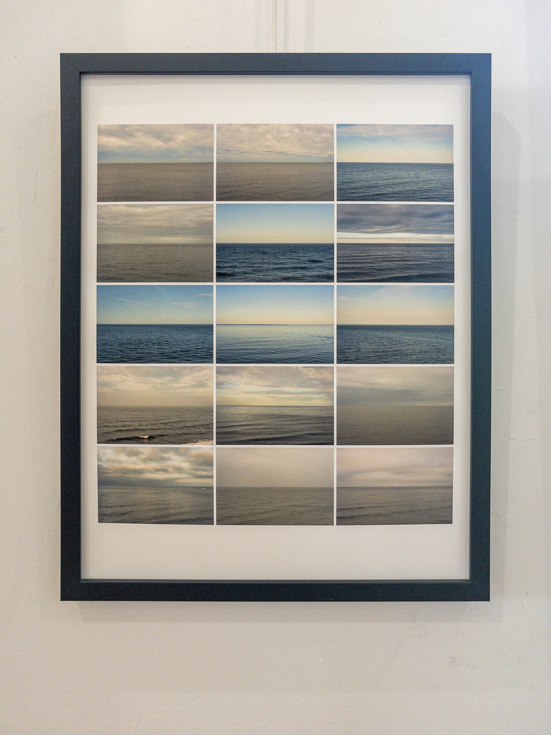 Framed photograph grid of the ocean horizon hanging on a wall in an exhibition.
