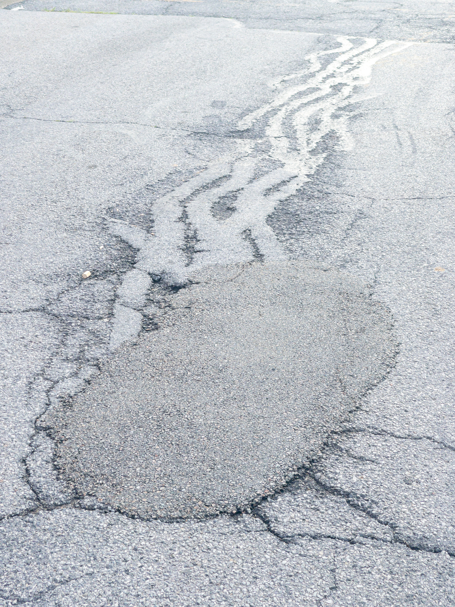 Large oval patch and curly crack patches in an asphalt road surface.