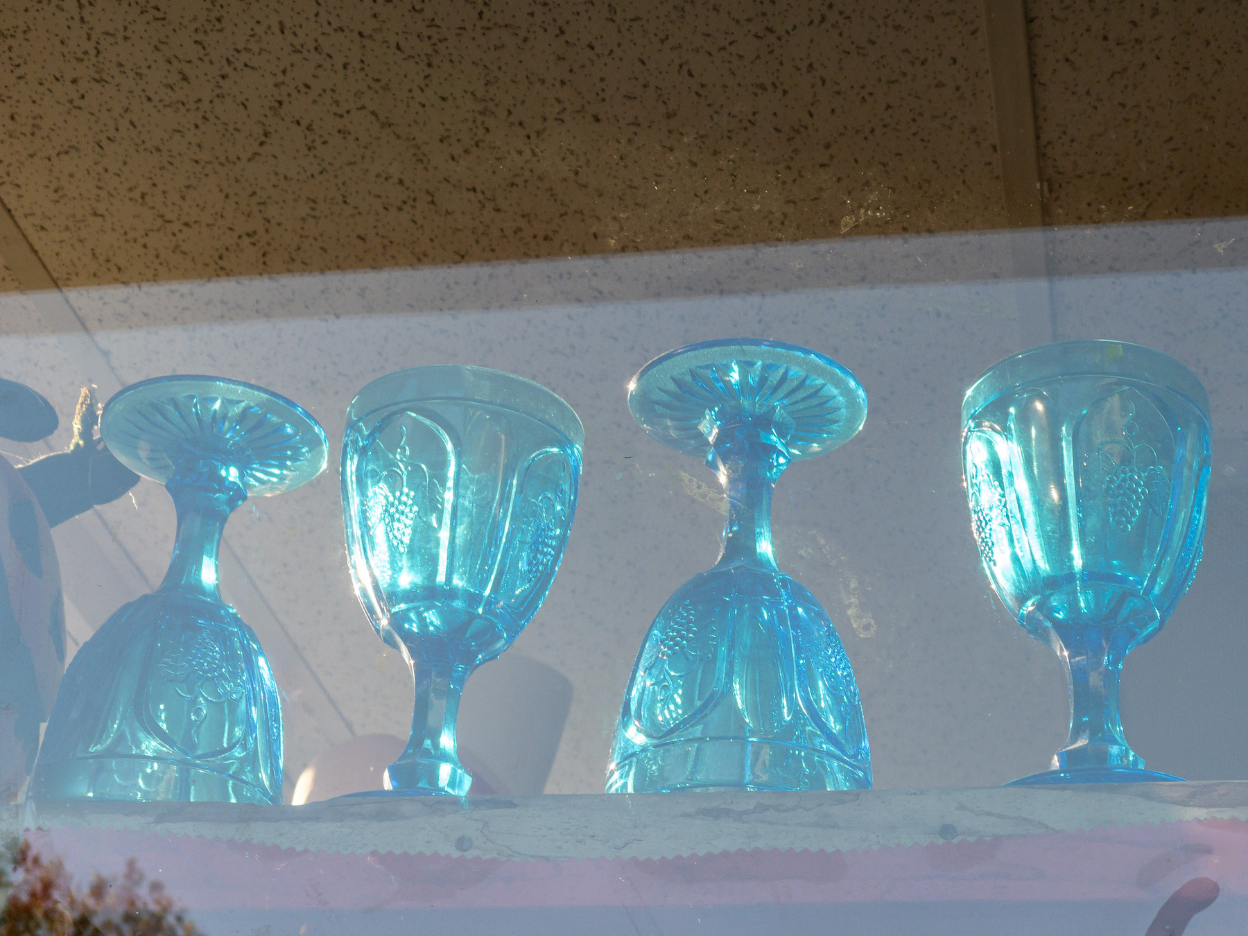Sunlit blue glass goblets on a glass shelf in the window of an vintage store.