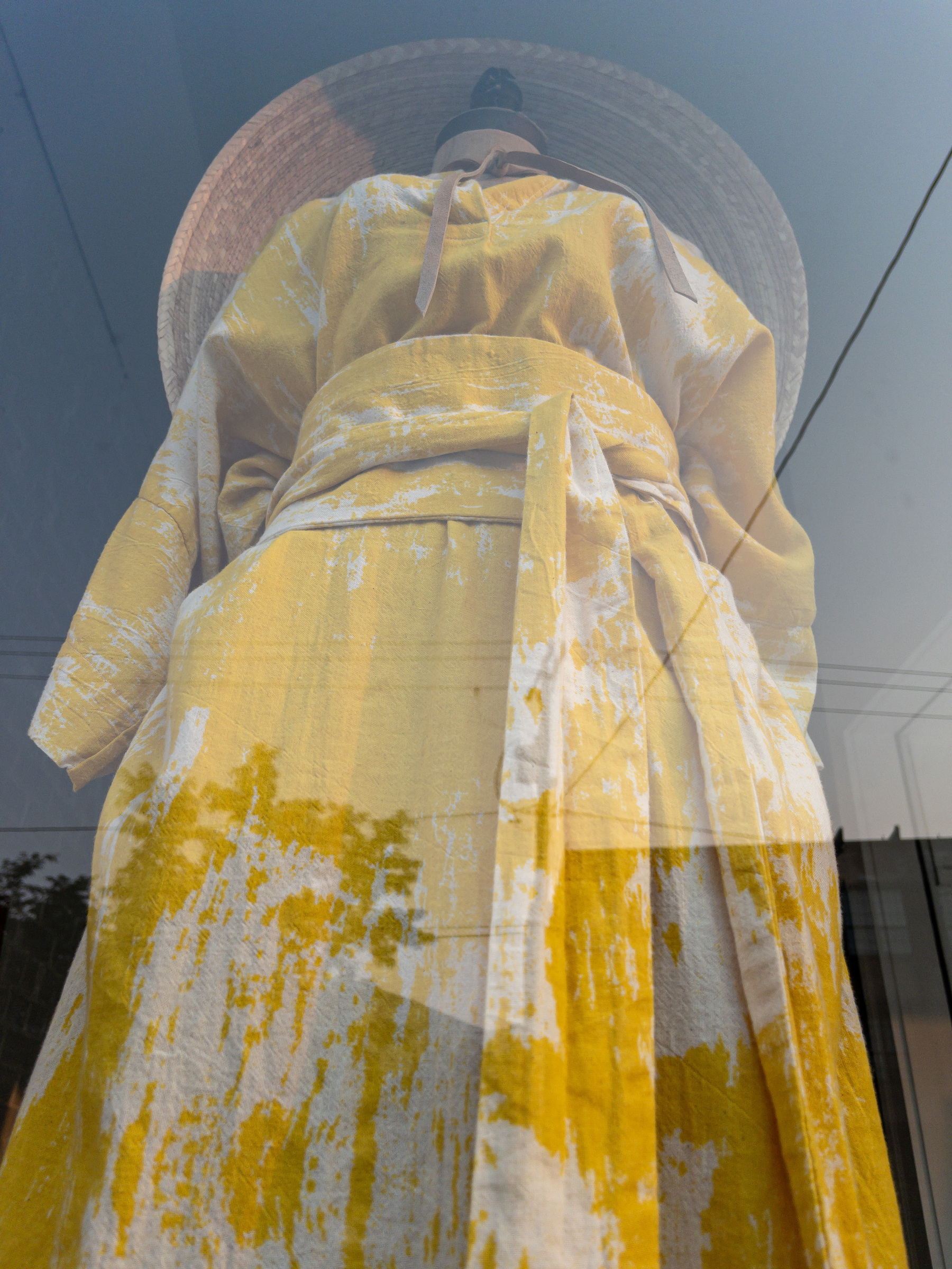 Yellow floral print dress, with sash at the waist, on a mannequin, with broad brimmed straw hat on top.