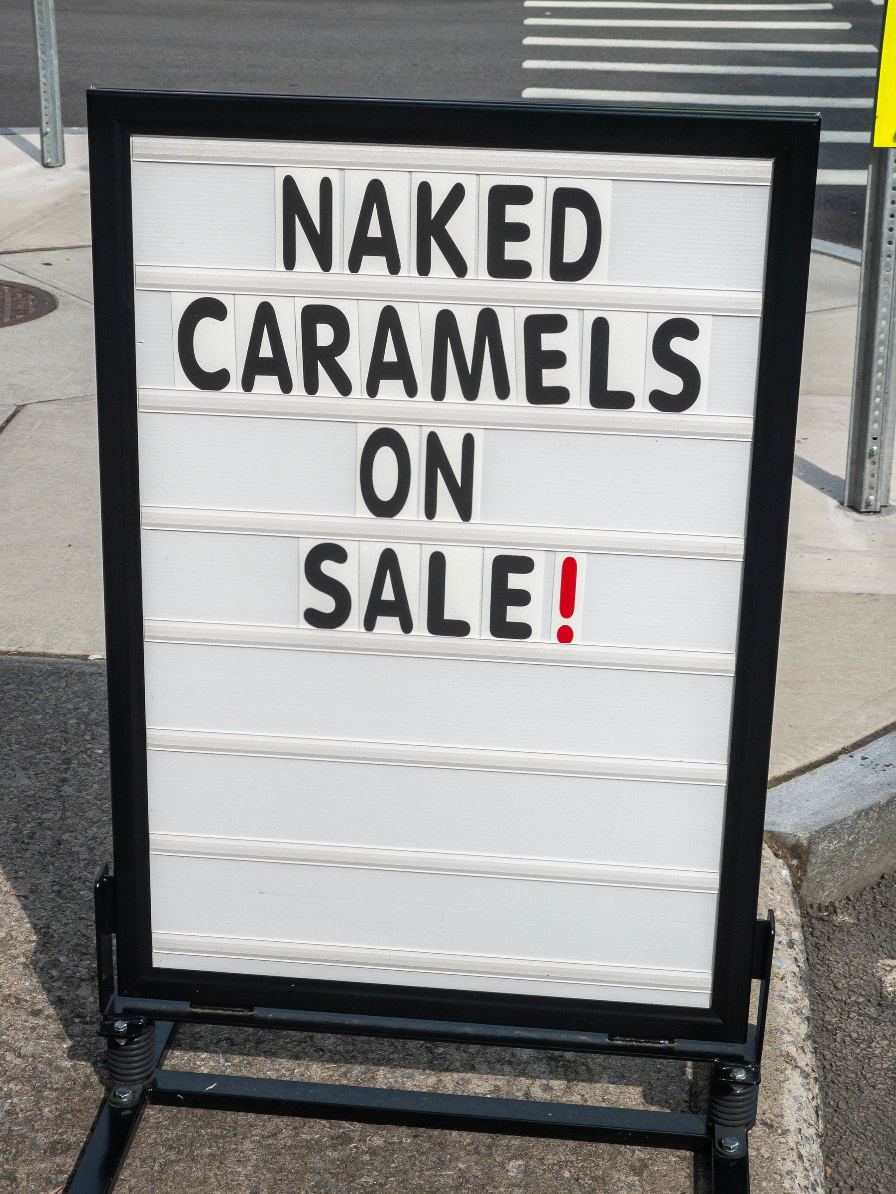 Sign on the sidewalk outside a shop with the words “NAKED CARAMELS ON SALE!”