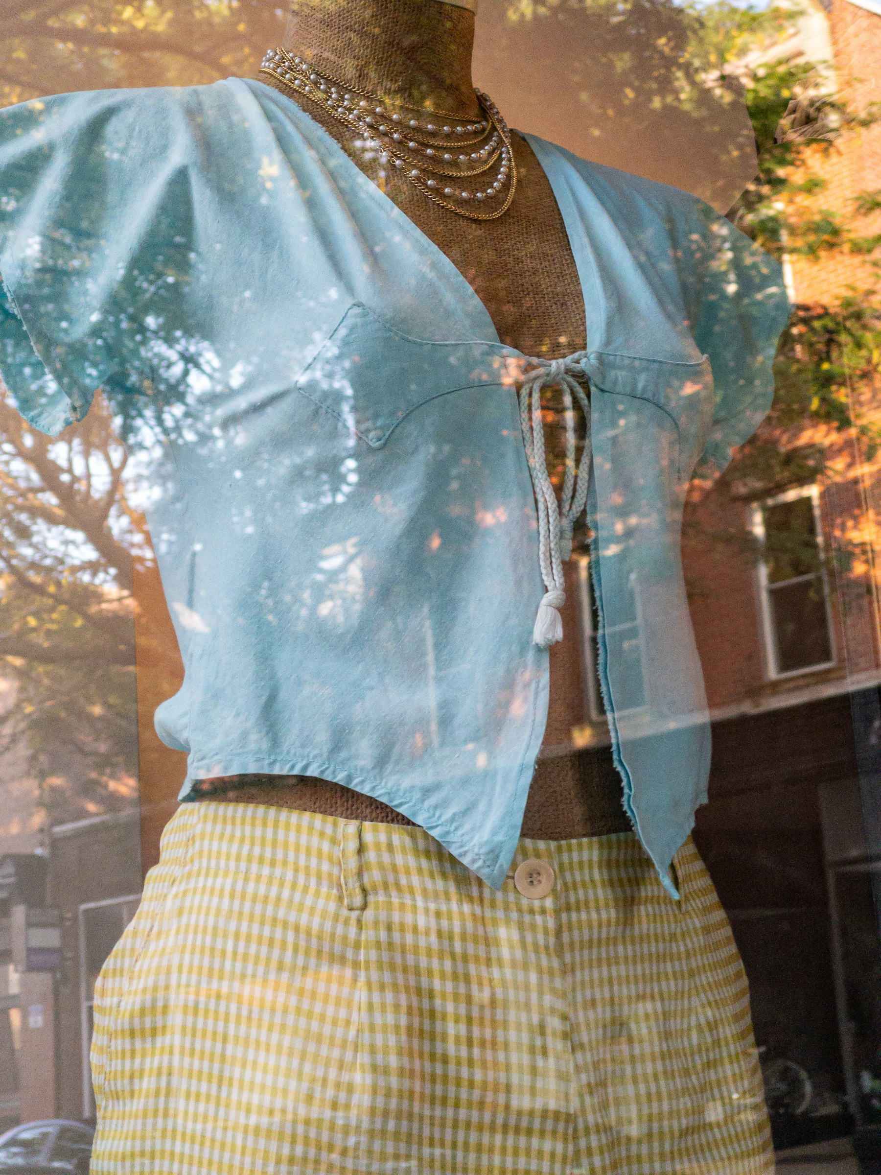 Woman’s light blue blouse open down the front, tied together at the bust line. Yellow seersucker pants. Displayed on an armless and headless mannequin form in a shop window.
