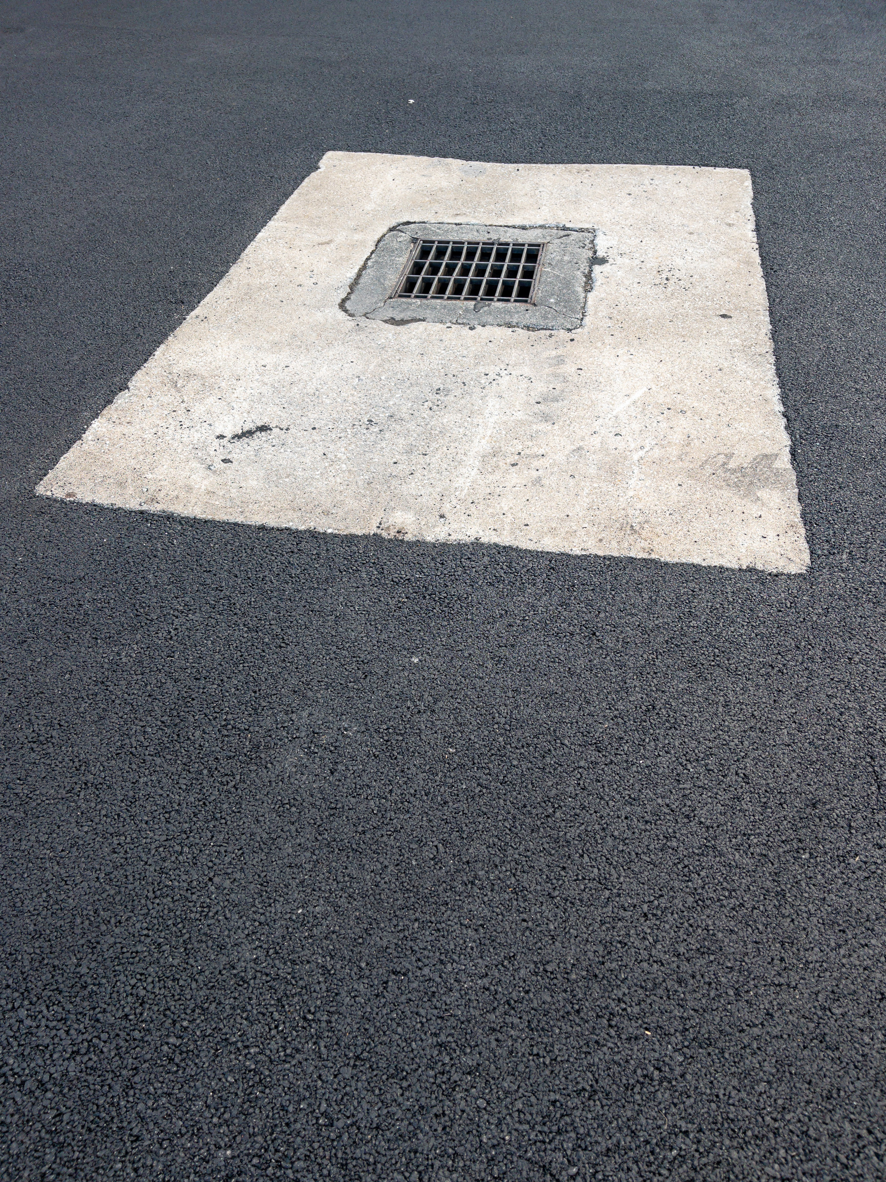 Rectangular concrete slab with drainage basin in the upper left corner surrounded by asphalt paving. Rectangle rotated to the right in the rectangular frame.