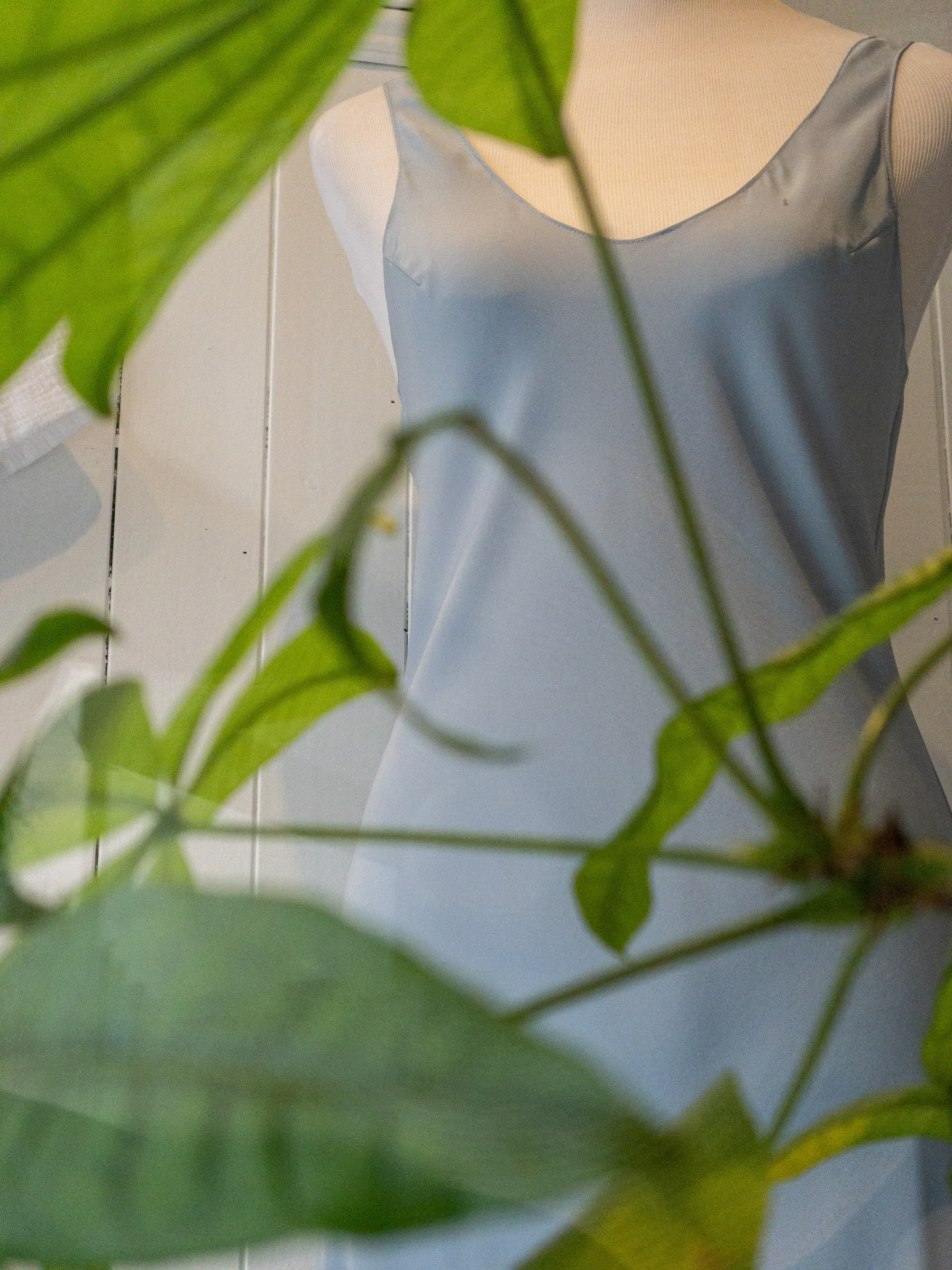 Gray silk sundress on mannequin form with plant leaf screen in front of it.