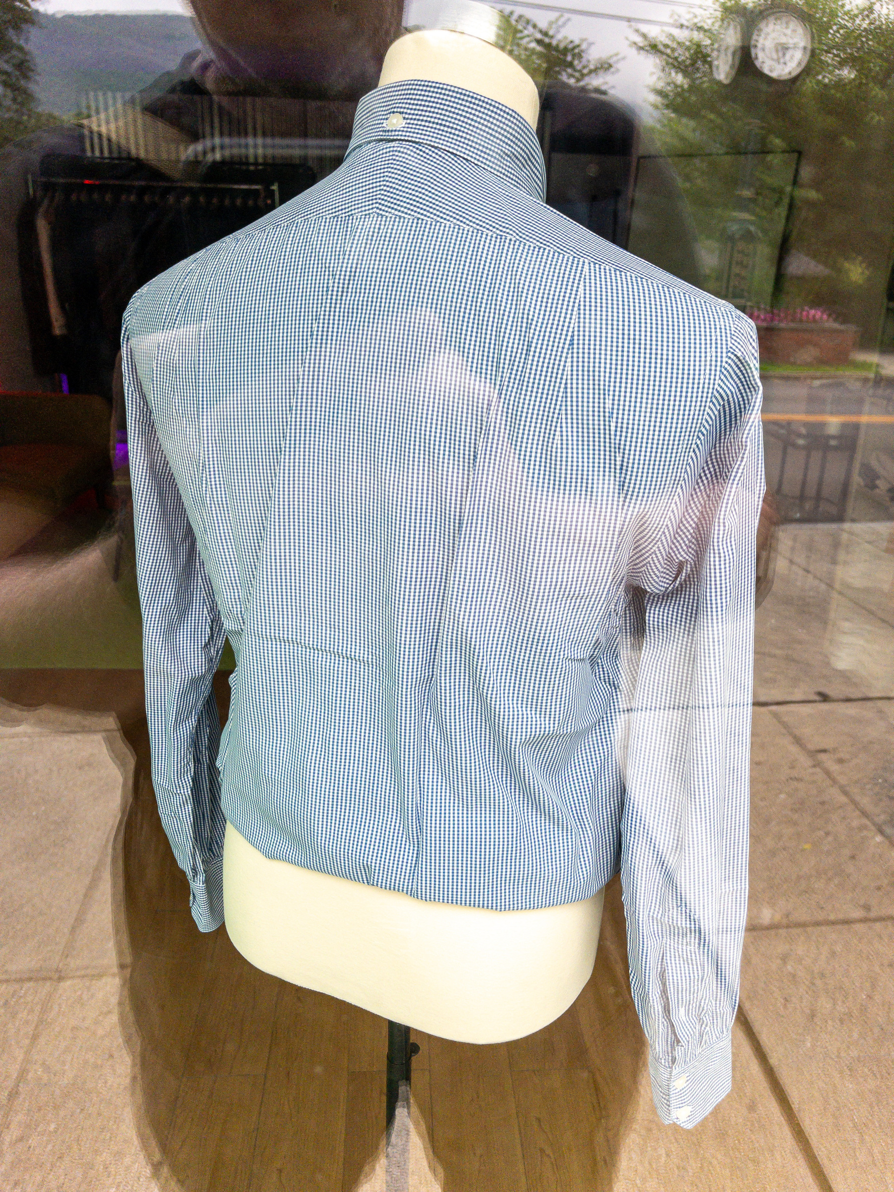 Back of a gray and white fine plaid men’s shirt on a bust mannequin in a fine tailoring shop.