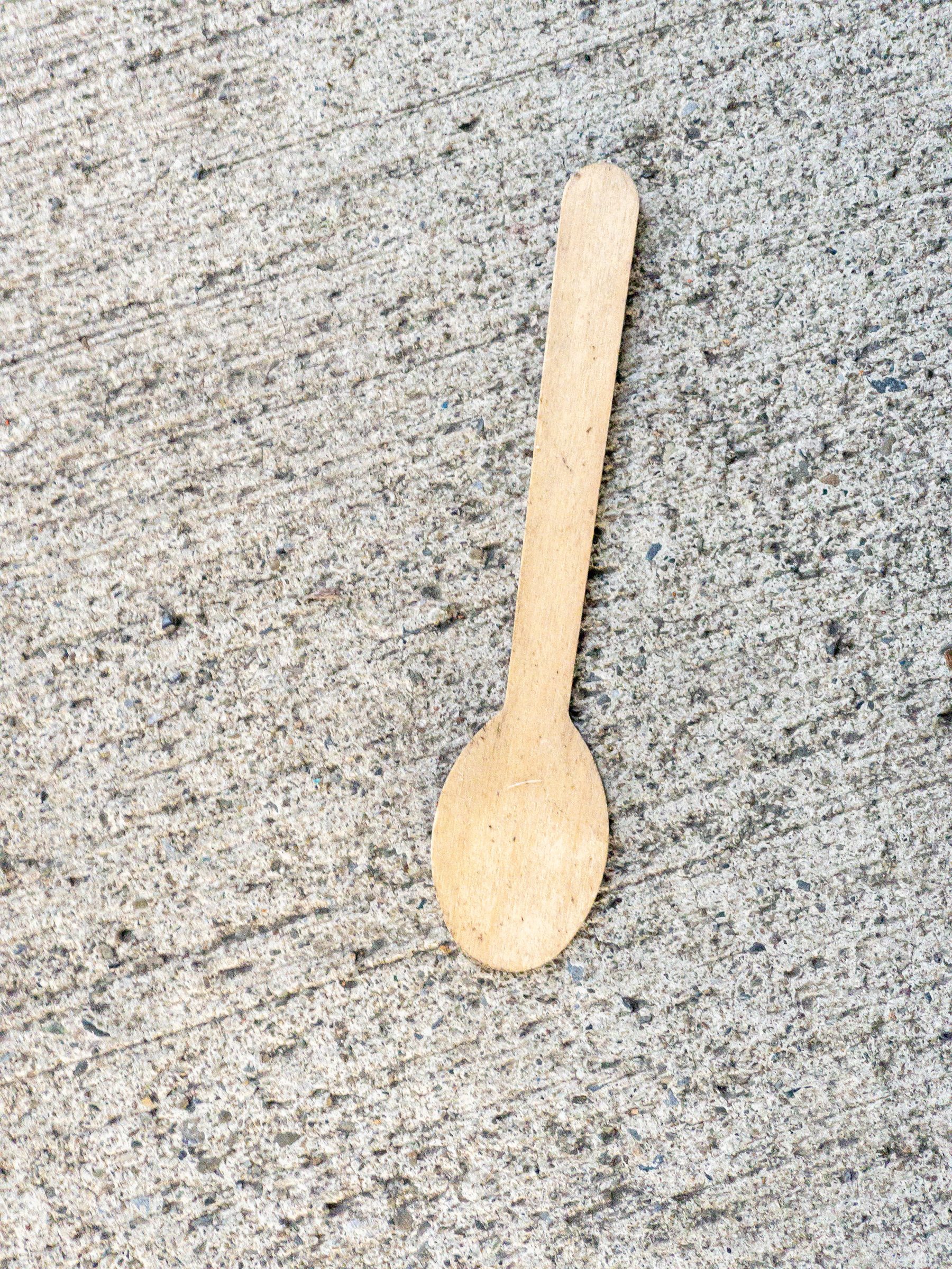Flat wooden ice cream spoon on concrete sidewalk.