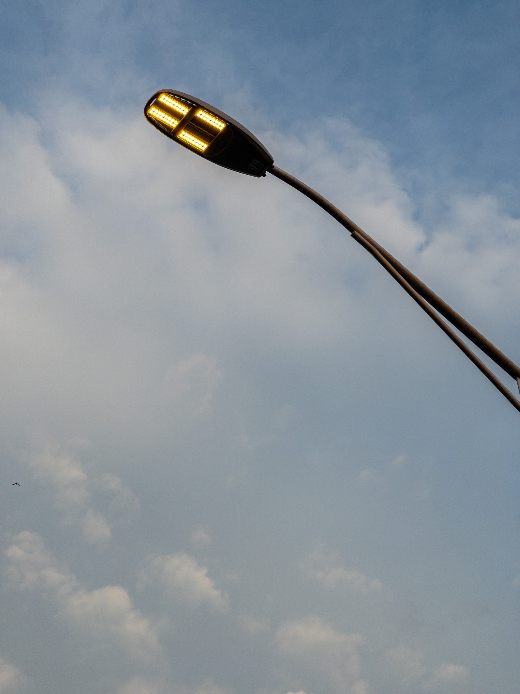 Streetlight against blue sky and clouds. Street light cuts across upper right corner of frame and is lit.