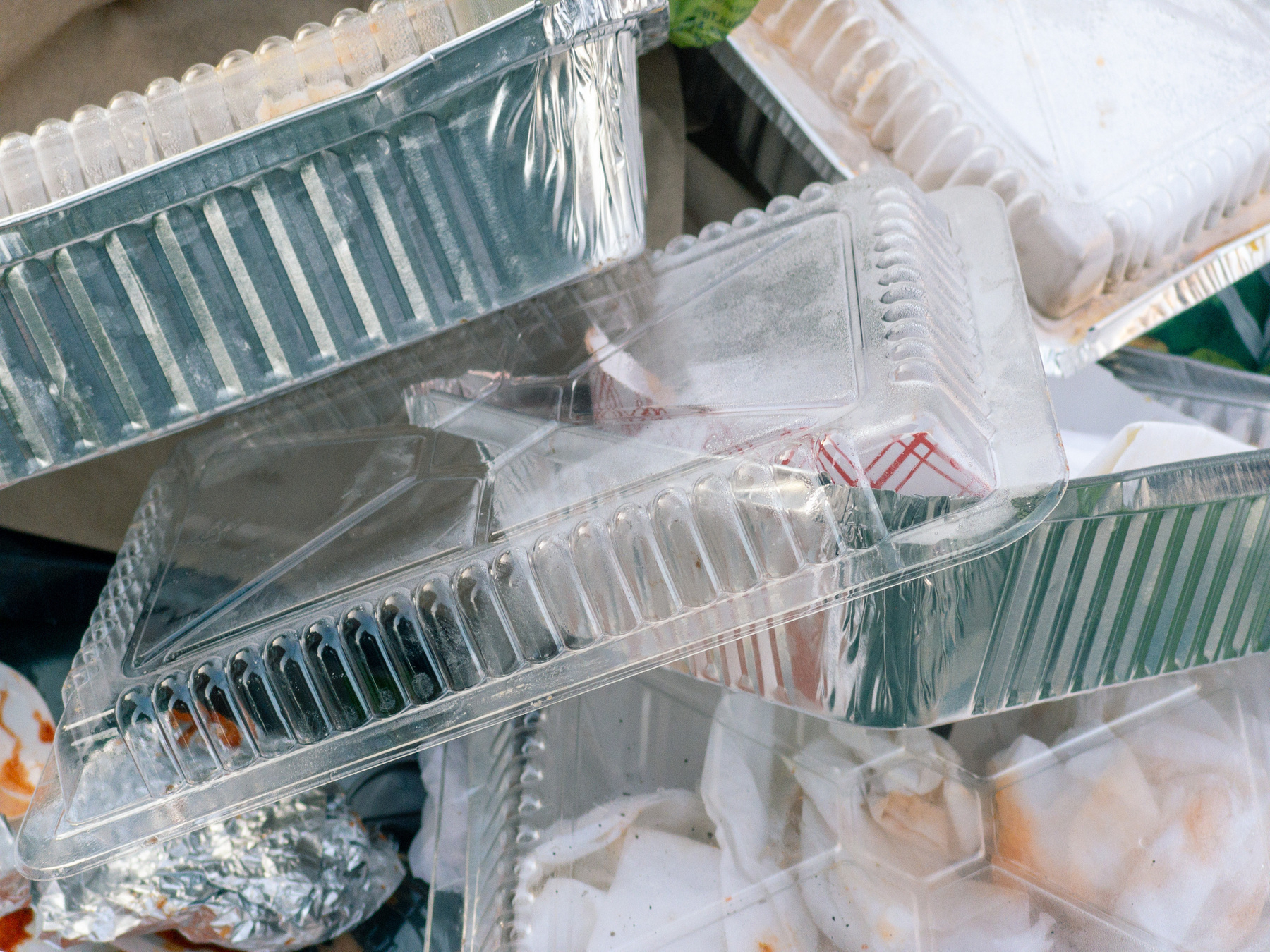 close up of plastic and aluminum takeout containers piled up in a trash receptacle