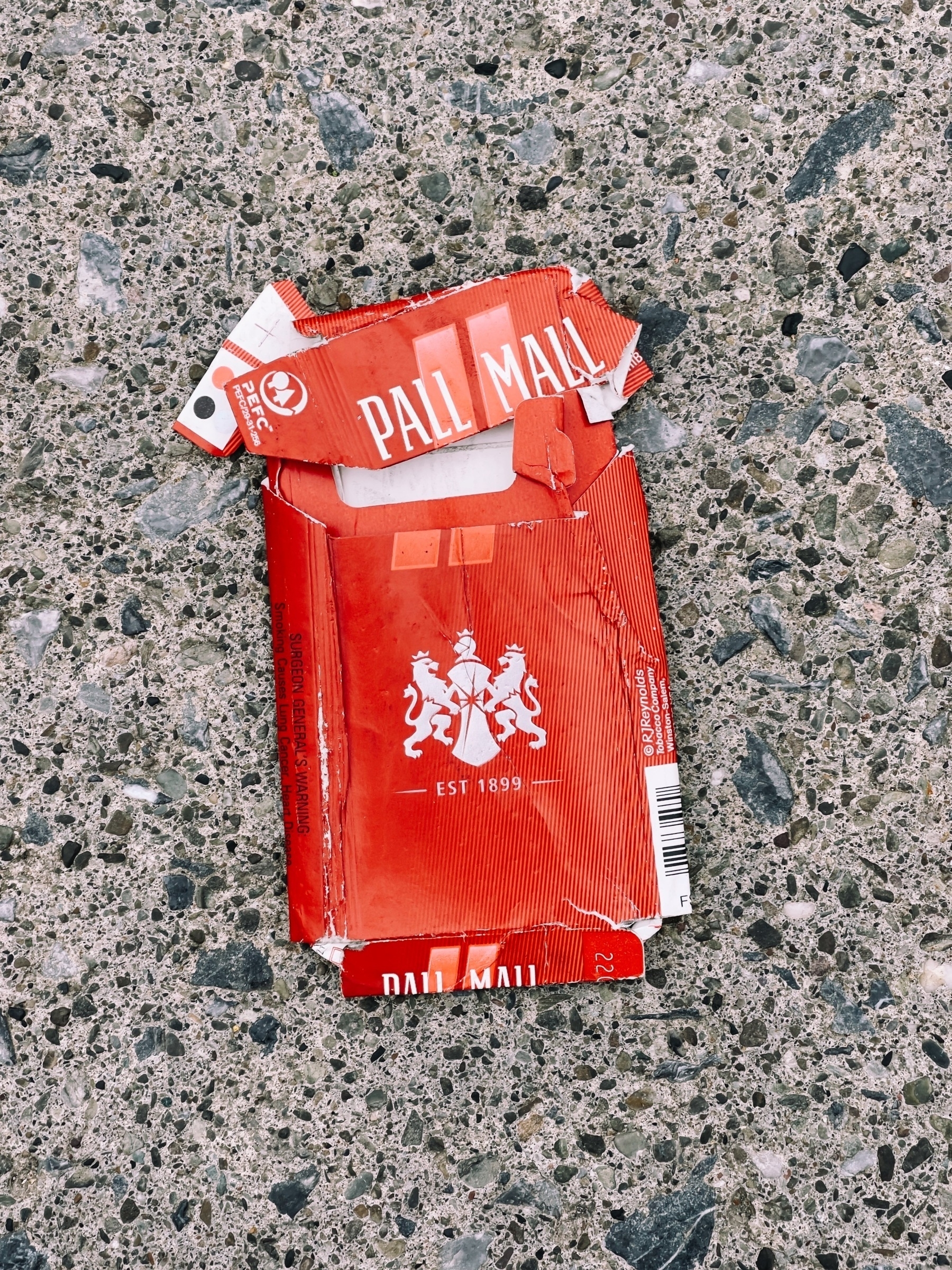 Orange-red Pall Mall cigarette packaging on concrete sidewalk.
