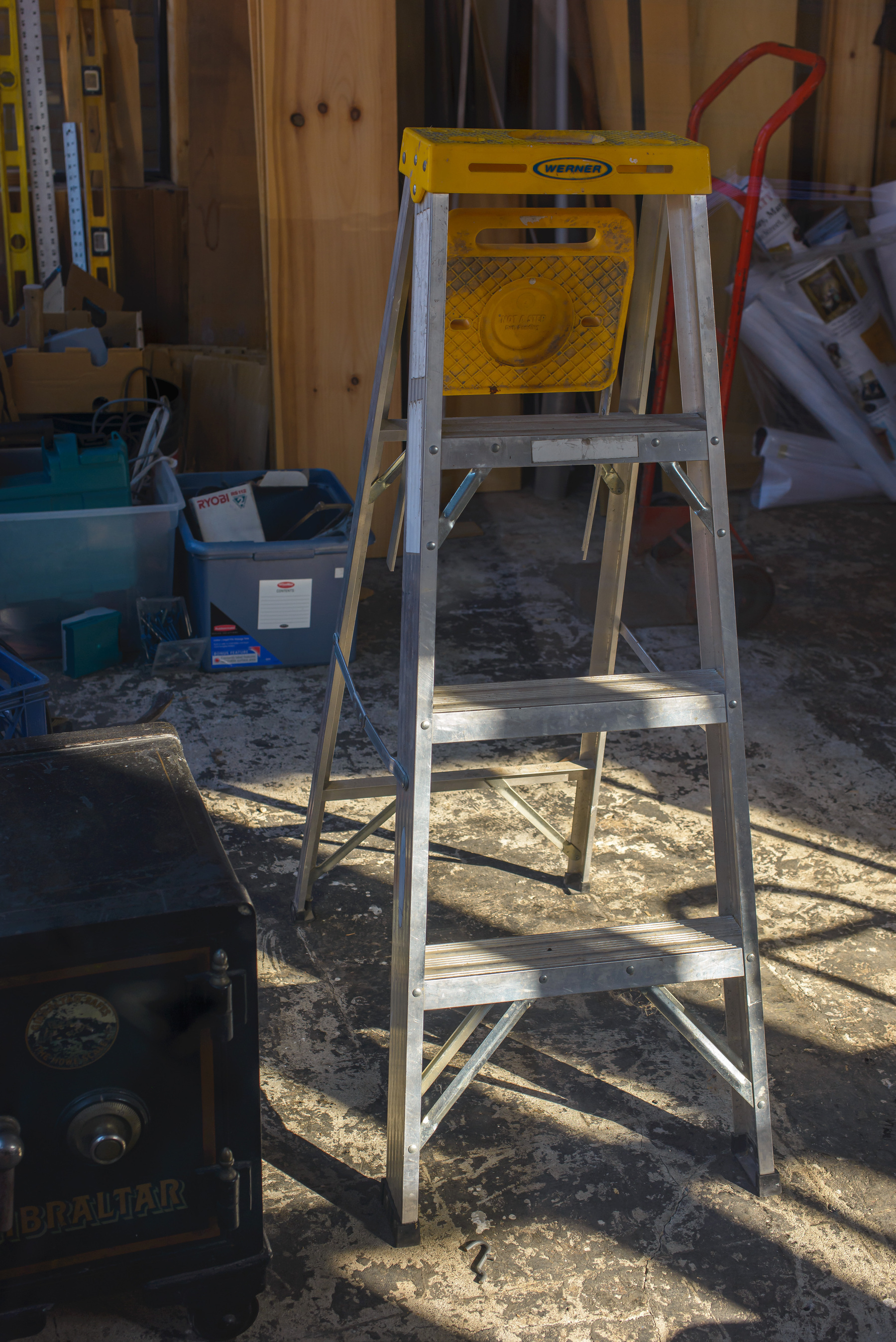 aluminum ladder in a space under construction, sunlight streaming in from the light across the floor and the lower two rungs of the laser